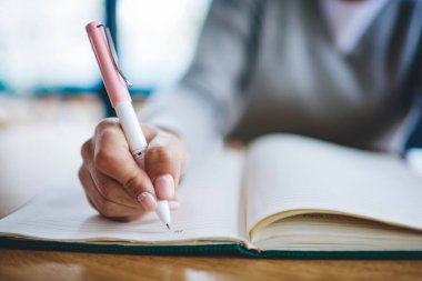 Pembe kalem tutan ve ev ödevi yapan defterin sayfalarına bilgi yazan bir kadının görüntüsü. Not defterine not defteri kayıt listesine not alan bir kadın.