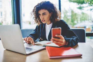 Modern uzayda dizüstü bilgisayarda kablosuz internet kullanan heyecanlı, kısa saçlı genç bir kadın dijital akıllı telefonu elinde tutarken, web sitesinde şok videosu izliyor.