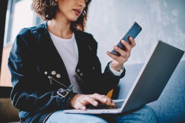 Akıllı telefonu elinde tutarken ve sosyal ağlarda bedava 4G internet bağlantısı kurarken dizüstü bilgisayara uygulama yükleyen sıradan giyinmiş genç bir kadının görüntüsü modern uzayda otururken görüntülendi.