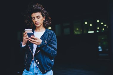 Kahveli genç bir kadın umumi ücretsiz 4G interneti kullanarak modern akıllı telefon cihazında sohbet etmeye gitti. Kafein içeceği içeren hippi kadın blogcu dijital cep telefonundan mesaj aldı