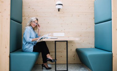 Elinde edebiyat kitabı tutan ve üniversite kampüsündeki tanıtım çekimlerinde dinlenirken kameraya bakan şık gözlüklü çekici genç kız portresi.