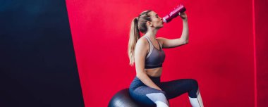 Denge için İsviçre topunun üzerinde dinlenen Kafkas fitness kızı ve modern spor salonundaki sıkı çalışma eğitiminden sonra ferahlatıcı su içen genç bayan atlet.