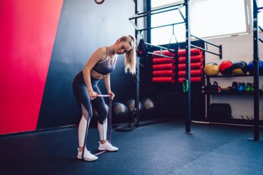 Sporcu kadın bacak ve eller kasları için egzersiz yapıyor, genç bayan sporcu, modern spor salonunda direniş bandıyla antrenman yapıyor, güç kavramı ve sağlıklı yaşam tarzı için motivasyon kavramı.