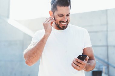 Olumlu sakallı adam, kulaklıkla müzik dinlerken cep telefonundan iyi haberlerle SMS mesajı aldı. 30 yaşındaki neşeli adam cep telefonu çalma listesinden şarkı seçiyor.