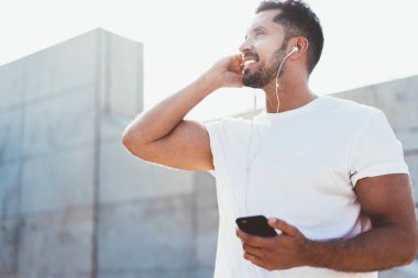 Başarılı sakallı adam elektronik kulaklıklar ve akıllı telefon uygulamaları kullanarak müziğin keyfini çıkartıyor. Şehir ortamında boş tişört konsepti ve etiket alanı için fotokopi alanı var.