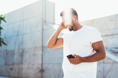 Yandan bakan, boş tişörtlü mutlu adam akıllı telefon uygulaması üzerinden sesli kitabı dinlediği için gülerken kulaklık takan, motivasyon içerikli web sitesinden kayıttan zevk alan pozitif bir erkek.