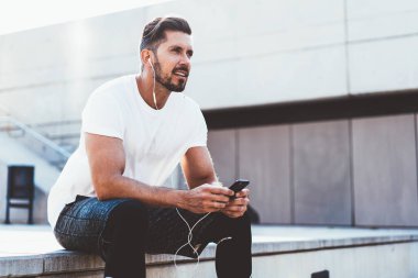 Yakışıklı bir erkek koşucu şık giyinmiş. Gözünü kaçırıyor. Cep telefonuyla 4G internete bağlanan ses tavsiyelerini dinliyor.