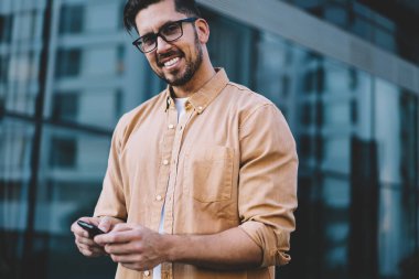 30 yaşındaki mutlu bir adamın yarım boy portresi dijital teknolojiyi kullanmaktan kaçarken kameraya bakıyor, Kafkas erkek blogcu modern cep telefonuyla iyi internet bağlantısı kuruyor.