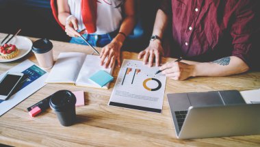 Ahşap masaüstünde oturan ve modern dizüstü bilgisayar kullanarak grafik çiziminin geliştirilmesi üzerinde çalışan iki tasarımcı görüşü kırpıldı. Ortak görevdeki öğrencilerin işbirliği