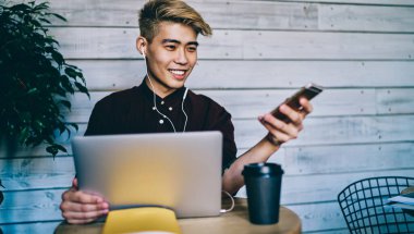 Modern kulaklıklarda cep telefonlarından müzik dinleyen Çinli genç adam kablosuz internet bağlantısı kullanarak dizüstü bilgisayara bağlandı. Laptop bilgisayarında çalışan neşeli Japon blogcu