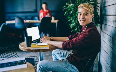 Modern uzayda oturan yeni bir girişim için dizüstü bilgisayarın başında çalışırken kameraya gülümseyen serbest giyinen başarılı Çinli genç adamın portresi