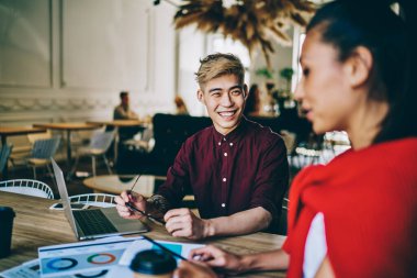 Mutlu Asyalı grafik tasarımcısı, çalışma sürecinde iş arkadaşıyla komik projeleri tartışırken gülüyor. Pozitif Çinli hippi arkadaşıyla dizüstü bilgisayarın başında otururken eğleniyor.