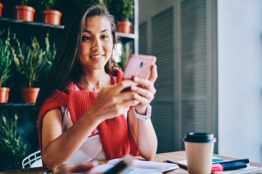 Gülümseyen Asyalı yenilikçi blog yazarı, sosyal ağlardaki takipçilerle sohbet ediyor, akıllı telefon cihazında. Cep telefonundan mesaj okuyan Çinli genç bir kadın.
