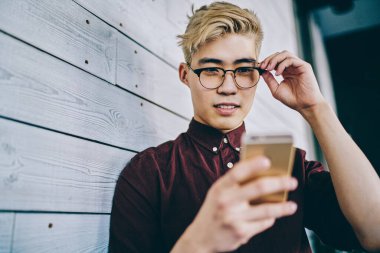 Asyalı hippi blogcu, internet sitesinde, duvarın yanında duran 4G interneti kullanarak haber okuyor. Akıllı telefondan sosyal ağlarda günlük kıyafetlerle sohbet eden Çinli genç adam.