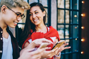 Sıradan giyinmiş neşeli Çinli hippi adamlar gülüyor ve akıllı telefonlarda komik profilleri tartışıyorlar şehir ortamında ayakta duruyorlar. Hücresel uygulamadan bahseden pozitif Asyalı arkadaşlar.