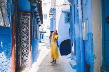 Renkli şehirde fotoğraf çeken, profesyonel kameralı güzel bir kadın - Fas 'ta yeni ekipmanlar test ediliyor, kadın fotoğrafçı tatillerde eski sokakların fotoğraflarını çekiyor.