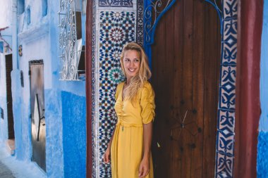 Deniz aşırı tatillerde gezen neşeli genç bayan gezgin, yabancı bir şehirde yaz macerası sırasında yabancı bir caddenin kenarındaki duvar resmi binasının yanında duran pozitif kadın gezgin Fas 'a.