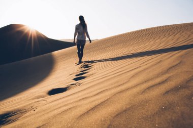 Doğada yaz akşamları vahşi Sahra Çölü 'nü keşfederken gündelik kıyafetleriyle gezen kadın turistin arka planda kalan görüntüsü. Kumda yürüyen kadın turist nefes kesici Safari' yi keşfediyor.