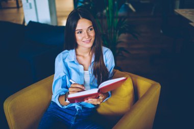 Pozitif hippi kız elinde eğitim kitabı tutuyor ve kapalı alanda kendini iyi hissediyor başarılı bir kadın üniversitede iç dekorasyonla oturuyor ve organizasyon planlamak için zaman harcıyor.