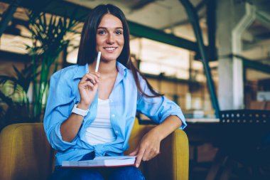 Kameraya bakan başarılı bayan öğrencinin portresi ve edebiyat camiasına makale yazma fikri. Rahat görünümlü, bilgi notlarıyla rahat koltukta oturan mutlu kadın.