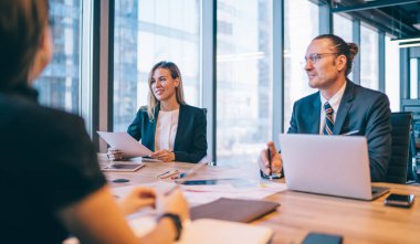 İşbirliği için ofiste yapılan beyin fırtınası sırasında masaüstünde oturan başarılı profesyonel meslektaşlar, şirkette çalışan pozitif erkek ve kadın girişimciler fikirler hakkında konuşuyorlar.