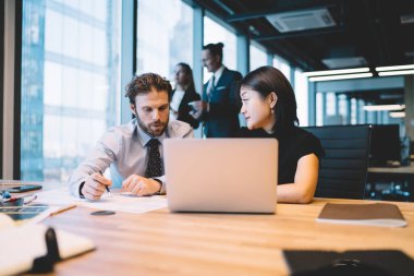 Ciddi erkek ve kadın finans uzmanları masaüstü yakınlarındaki muhasebe sürecinde modern dizüstü bilgisayarla bilgi kontrol ediyorlar, olgunlaşmış çeşitli iş arkadaşları başlangıç projesi raporları hakkında danışmanlık yapıyorlar