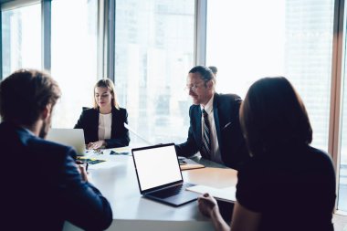 Bir grup iş adamı ofis masasında dizüstü bilgisayarlı ve boş ekran alanlı bir şekilde oturuyorlar. Metin reklamları için işbirliği yapıyorlar ve birlikte beyin fırtınası yapıyorlar. Zeki meslektaşlar içeride iş birliği yapıyorlar.