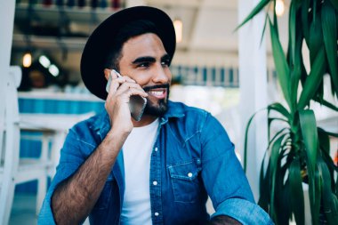 Moda siyah şapkalı mutlu İspanyol adam iyi bir internet bağlantısı olan şehir ortamında akıllı telefon sohbetinin tadını çıkarıyor.