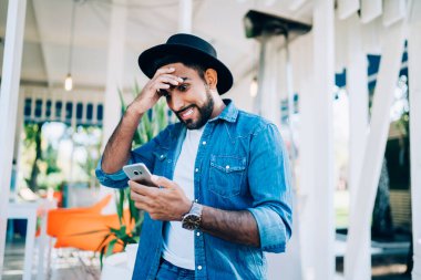 Kot giyim kuşamı giymiş hayret verici hipster blogcusu akıllı telefon zımbırtısında düşük şarjlı pil olduğu mesajıyla şok oldu. Şık kot gömlekli şaşırmış adam.