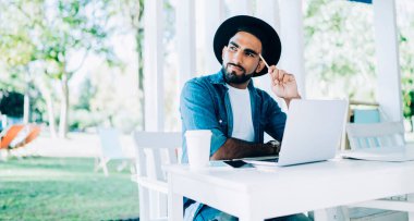 Düşünceli Türk değişim öğrencisi, üniversite kafeteryasında modern dijital dizüstü bilgisayar ve uzaktan çalışma konseptiyle sınav savunması için dil öğrenme üzerine kafa yoruyor.