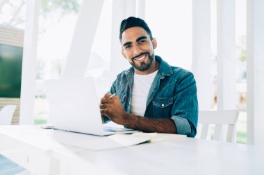 Yüzünde sevimli bir gülümseme olan neşeli bir hippi portresi açık dizüstü bilgisayarla internetteki işine ara veren İspanyol erkek serbest çalışan iyi bir internet bağlantısı olan sokak kafeteryasında oturuyor.