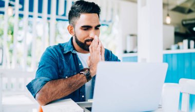 Düşünceli erkek metin yazarı blog yazarları için internet sitesindeki makalesi hakkında yorum okuyor. Alınan bilgilerle stresli hissediyorlar. Düşünceli bir adam dizüstü bilgisayarda bilet almada sorun yaşıyor.