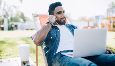 Elektronik kulaklıklarda yakışıklı İspanyol milenyumu. Ses kitabı ve dizüstü bilgisayarla öğrenmek için hayal kuruyor. İnternet bağlantısı kullanıyor.