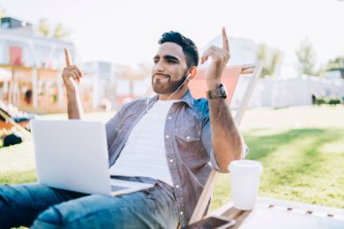 Kampüste boş zamanlarında elektronik kulaklıkla müzik dinleyen modern laptopta internete bağlanan, dans eden elleri dışarıda dinlenen genç hippi.