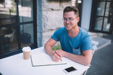 Üniversite web siteniz veya diğer reklam metinleriniz için boş ekran alanına sahip modern cep telefonu aygıtı, olumlu erkek öğrencilerin açık hava kafeteryasında not defteriyle oturarak zaman geçirmesi