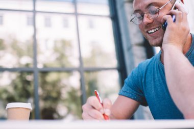 Cafe 'nin başarılı erkek müdürü teslimat zamanını kontrol ettiği için sağlayıcıyı arıyor. Akıllı telefon konuşmaları sırasında notlar alıyor. Gözlüklü mutlu adam cep telefonuyla konuşuyor.