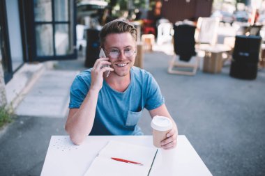 Klasik gözlük takan neşeli erkek öğrenci akıllı telefondaki cep telefonu uygulaması ve iletişim konseptiyle en iyi arkadaşa telefon çalışmasından keyif alarak göz koruması sağlıyor.