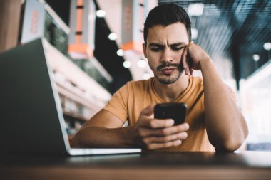 Şaşırmış erkek programcı, dizüstü bilgisayarda yazılım geliştirmek için yeni görevlerle e-posta aldı. Sıradan giyinen genç adam, cep telefonu aygıtındaki çevrimiçi sorunla karıştırıldı.