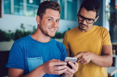 En iyi arkadaşıyla boş zamanlarını geçirirken kameraya gülümseyen neşeli beyaz erkek blog yazarının yarım boy portresi, akıllı telefon cihazıyla e-posta kutusunu kontrol eden bin yıllık adam.