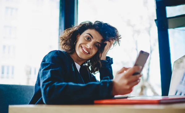 一位迷人的嬉皮士女郎的画像 她一边笑着 一边看着相机 一边用智能手机发短信 在笔记本电脑上远程工作 — 图库照片