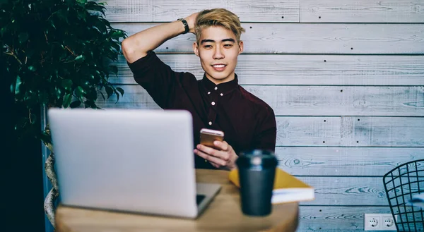 Asyalı hippi öğrenci elinde akıllı telefonu dinlerken ve internet sitesinde kablosuz internete bağlı videolar izlerken. Çinli genç serbest çalışan netbook 'ta arıza yaptı.