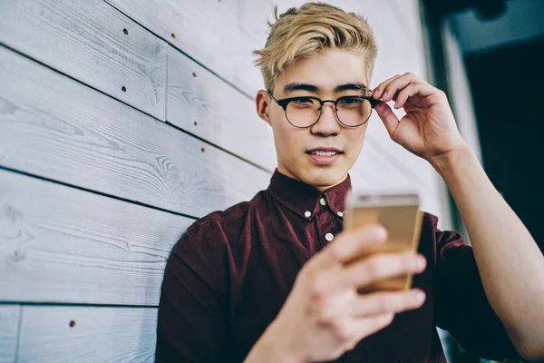 Asyalı hippi blogcu, internet sitesinde, duvarın yanında duran 4G interneti kullanarak haber okuyor. Akıllı telefondan sosyal ağlarda günlük kıyafetlerle sohbet eden Çinli genç adam.