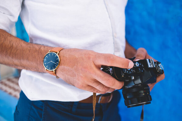 Обрезанное изображение стильного мужчины журналиста, тестирующего ретро-камеру для редактирования фотографий во время путешествия, модного туриста с носимыми механическими наручными часами, проверяющего винтажное оборудование с фотографиями
