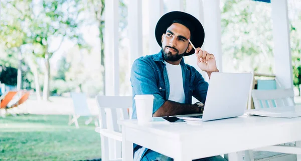 Düşünceli Türk değişim öğrencisi, üniversite kafeteryasında modern dijital dizüstü bilgisayar ve uzaktan çalışma konseptiyle sınav savunması için dil öğrenme üzerine kafa yoruyor.