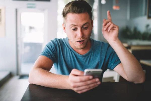 Smart millennial hipster guy holding finger up surprised with creating good idea for online publication on website for genius,young man amazed with solution for internet connection on cellphone gadget