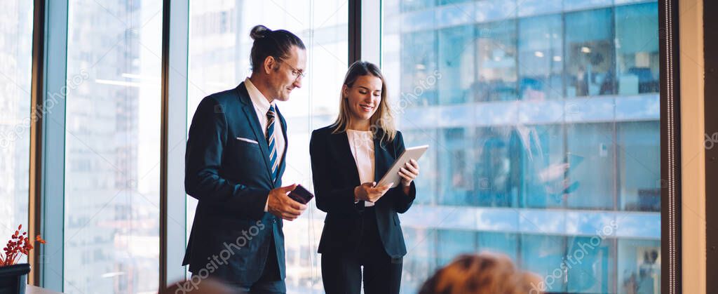 Successful male and female directors in formal wear reading news on web page during break from office cooperation, caucasian partners using company internet connection for communication via touch pad