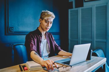 Gündelik giysiler giymiş yaratıcı Japon grafik tasarımcısı modern dizüstü bilgisayardaki internet sitesinde kablosuz internet kullanıyor. Netbook 'ta oturan ve serbest çalışan Çinli genç adam