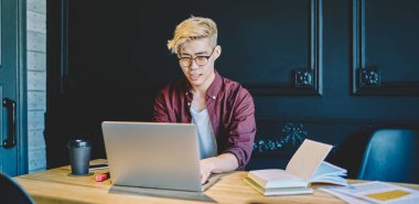 Dizüstü bilgisayar başında oturan ve birlikte çalışmanın modern alanında uzaktan çalışan şık Japon genç adam. Çinli hipster adam internet üzerinden yazılım güncelliyor ve arama bilgileri için kablosuz internet kullanıyor.