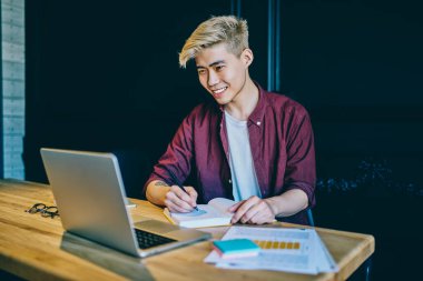 İnternet sitesinde webinar izlerken gülen ve not defterine notlar yazan pozitif Çinli hippi. İnternet sitesinden komik haberler okuyan neşeli Asyalı genç adam.