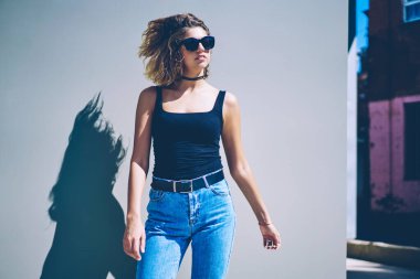 Güneşli yaz gününde duvarın yanında dikilen günlük kıyafetli genç hippi kız, şehirde yürüdükten sonra şehir merkezinde dinlenen modaya uygun kot giysili çekici beyaz kadın gezgin.